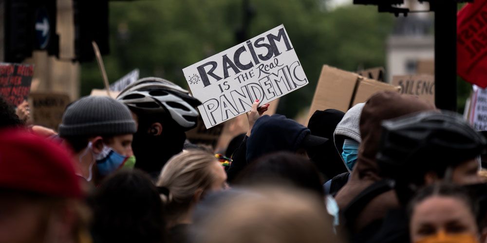 protestors at a Black Lives Matter march with the sign "Racism is the real pandemic"