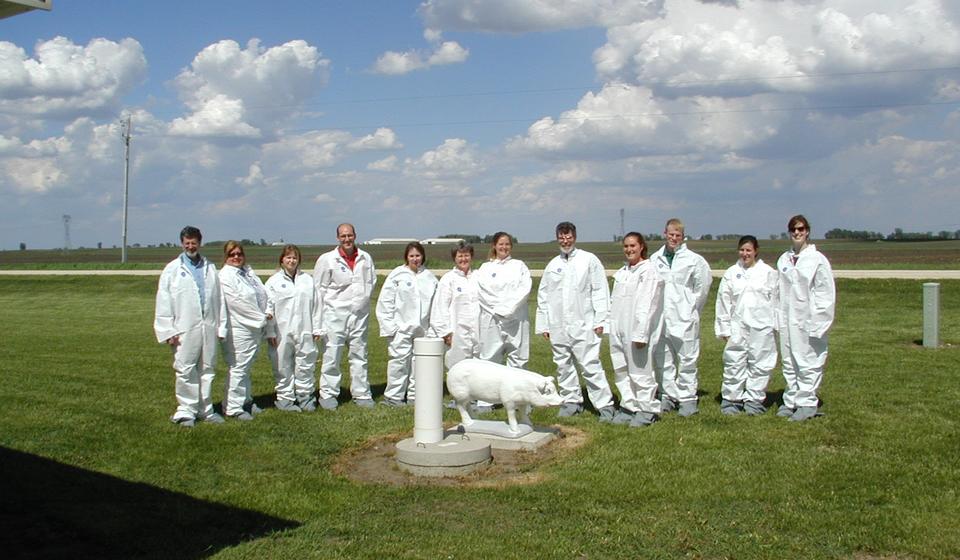 A group of people in protective gear on a farm smiling at the camera